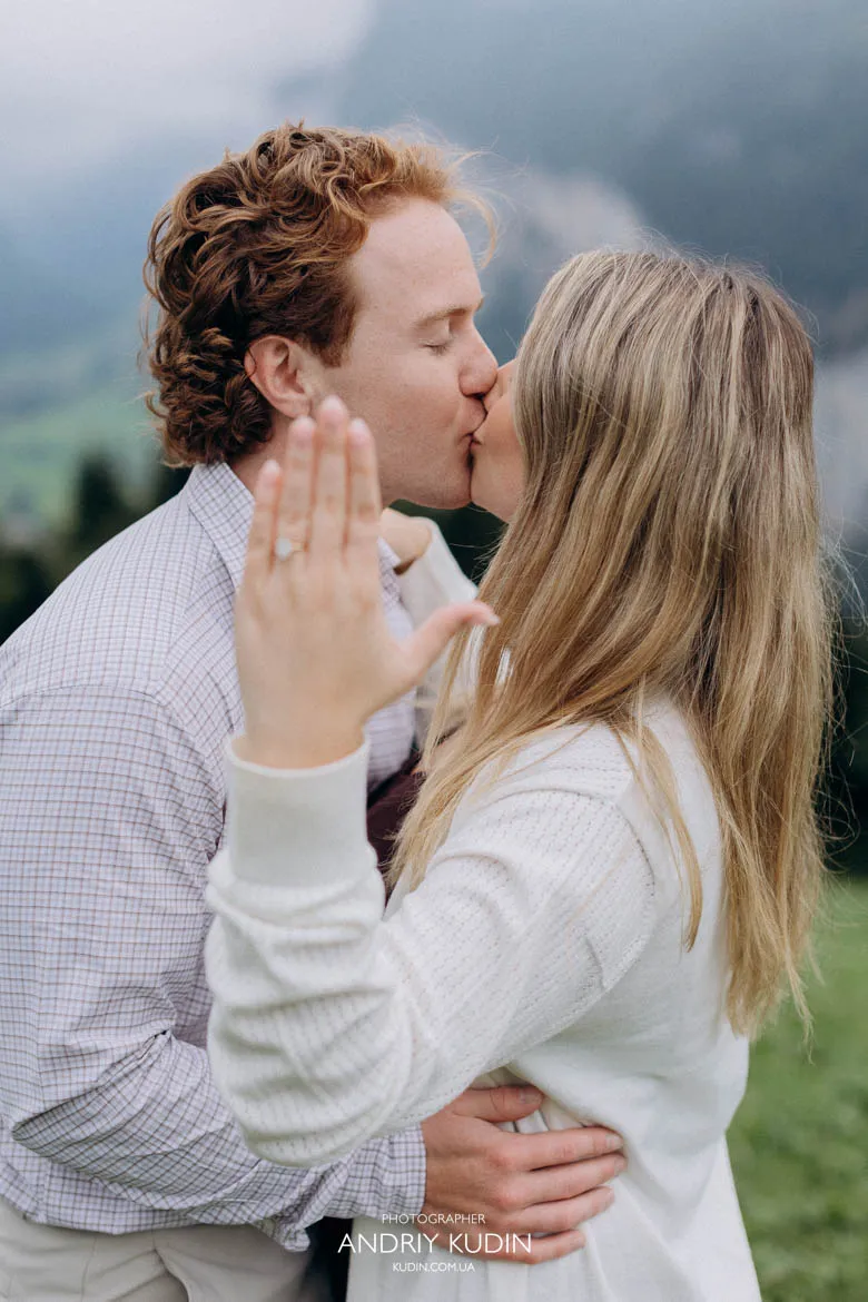 Newly engaged couple kissing with hand and ring in foreground in Lauterbrunnen. Photo by switzerland proposal photographer.