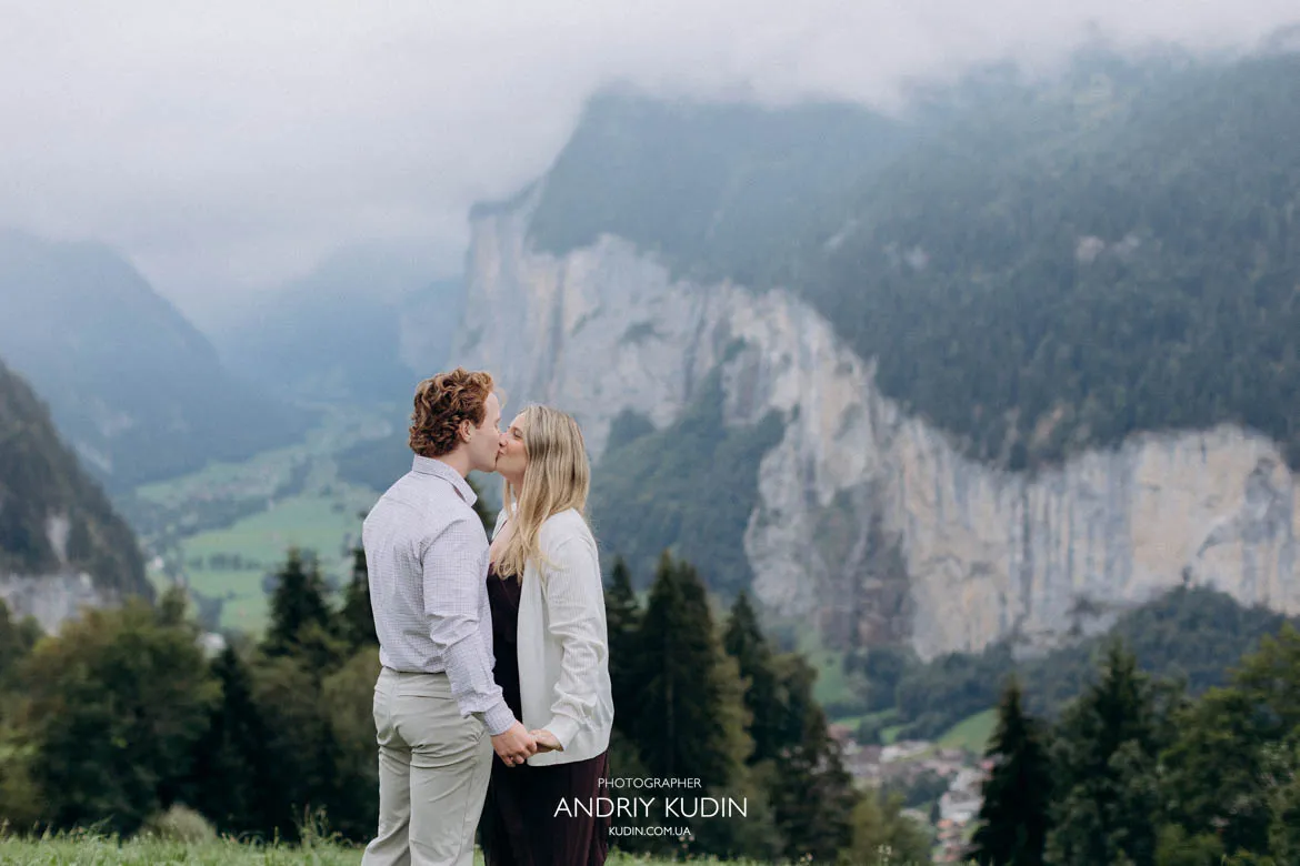 Engaged couple kissing outdoors with dramatic cliffs and Lauterbrunnen Valley in background. Photo by switzerland proposal photographer.